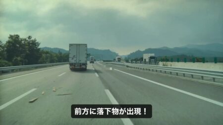 Wood plank lying in the middle of the expressway lane, just past the truck ahead