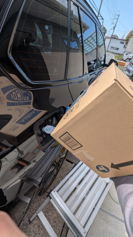 Tipping the AdBlue carton into the filler neck, supported on a step ladder