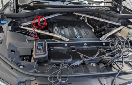 Engine bay of a BMW X3 F25 with the red charger clip attached to the positive charging terminal circled in red