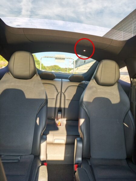 Looking up at the third-row ceiling of a Tesla Model YL. The red circle marks the rear map light switched on in daylight