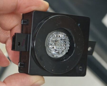 The rear map light unit removed from a Tesla Model YL, with interior fabric pinched under its cover