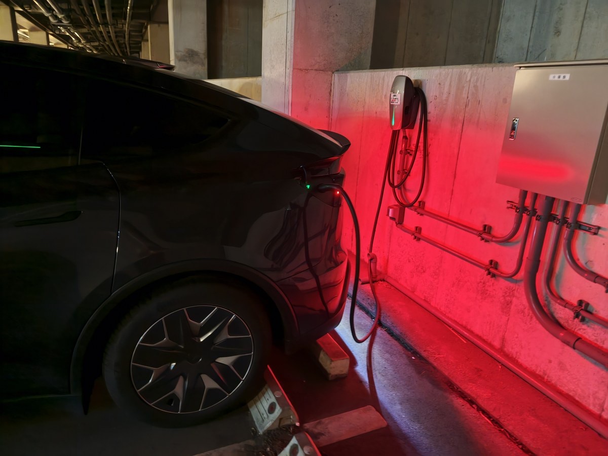 夜の駐車場でデスティネーションチャージャーにつないだテスラ Model YL