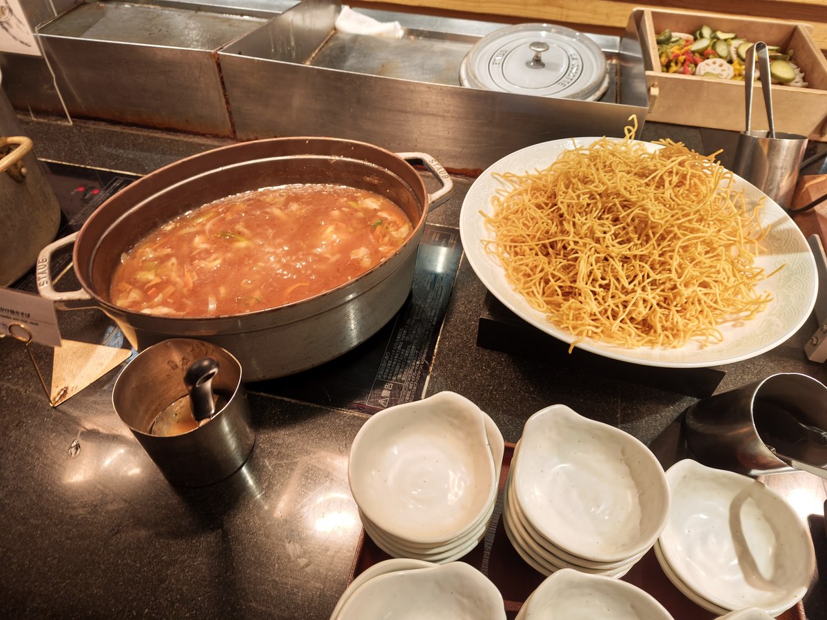 スープの鍋と揚げ麺、取り皿が並ぶビュッフェ台