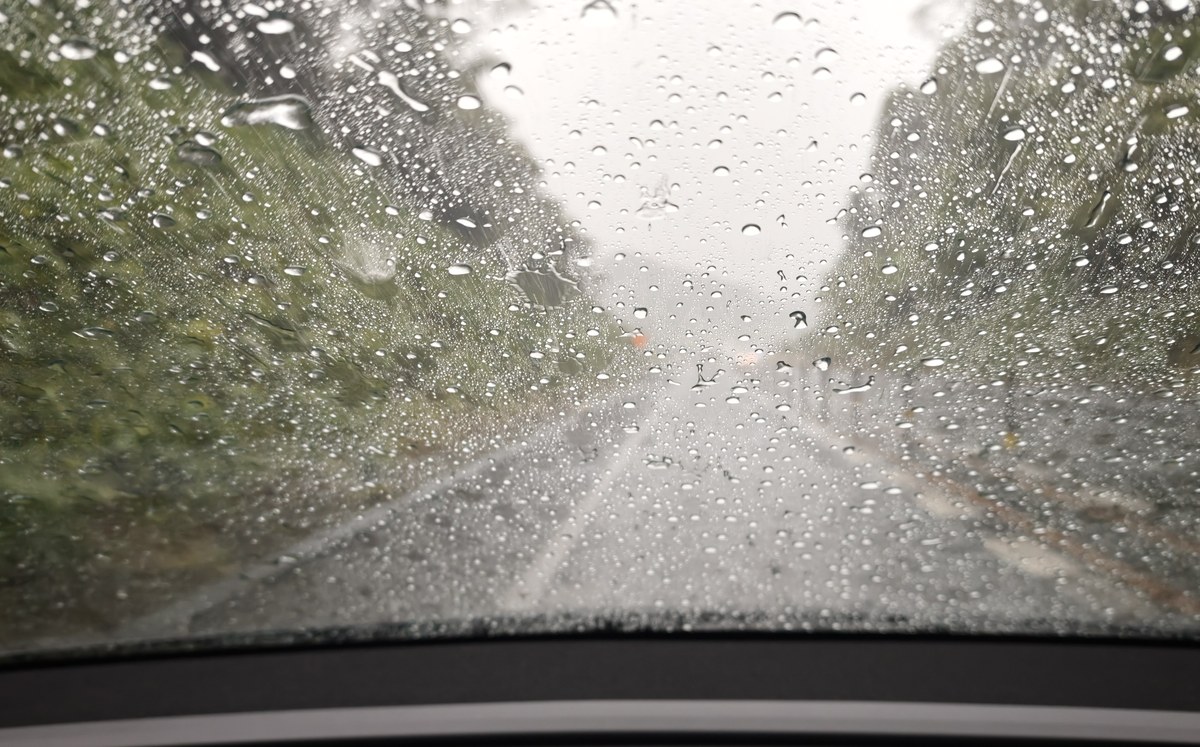雨粒だらけのフロントガラス越しに見る高速道路。周囲は緑の山
