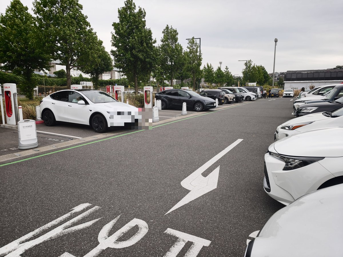 北九州スーパーチャージャーのストール。手前に白いテスラが充電中、ナンバープレートにはモザイクをかけている